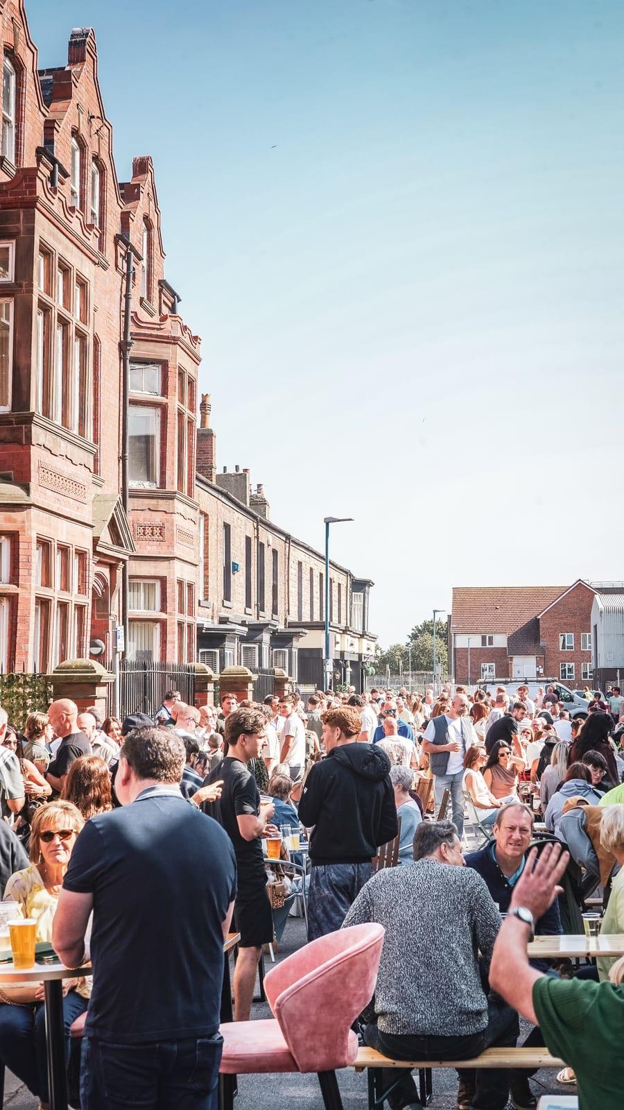Packed street event with crowds at outdoor tables in the sun