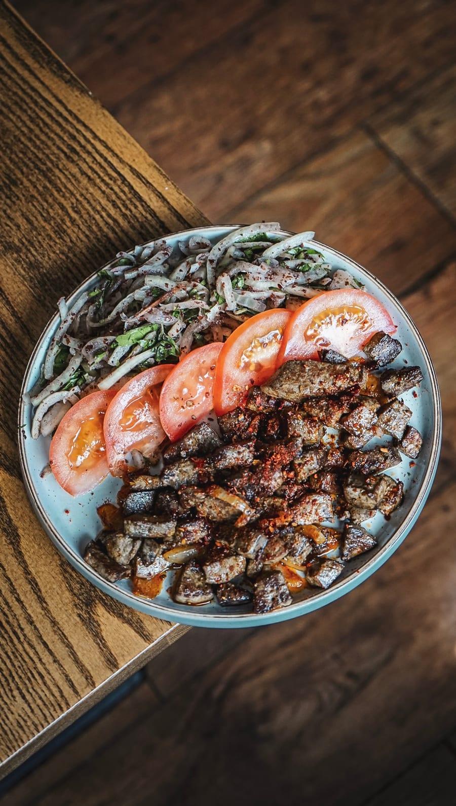 Plate of spiced lamb with tomatoes and onion salad on a wooden table