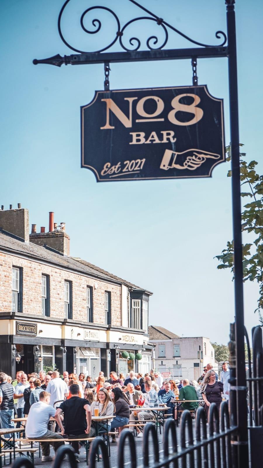 The No.8 Bar sign above a packed street of people at outdoor tables